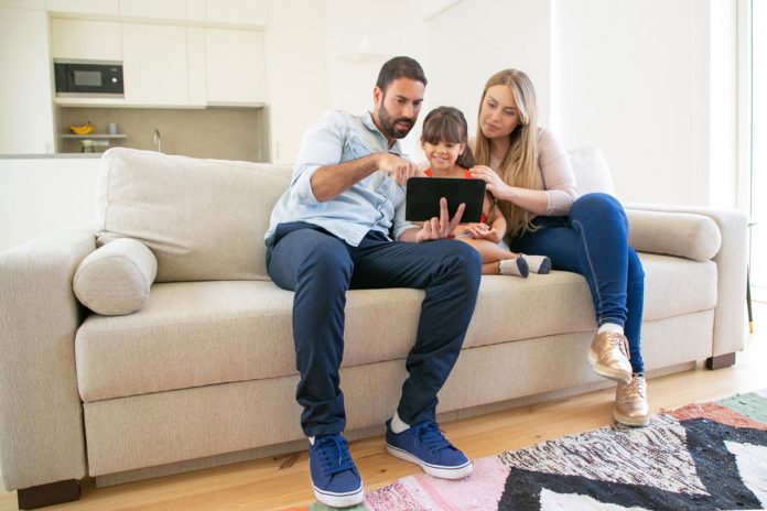 Gastos nas férias: 6 dicas para não estourar o orçamento da família; mãe, pai e filha olham para tela de ipad