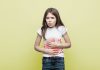 Criança com intestino preso: o que fazer para resolver esse problema; menina apoia mãos sobre barriga e faz expressão de dor