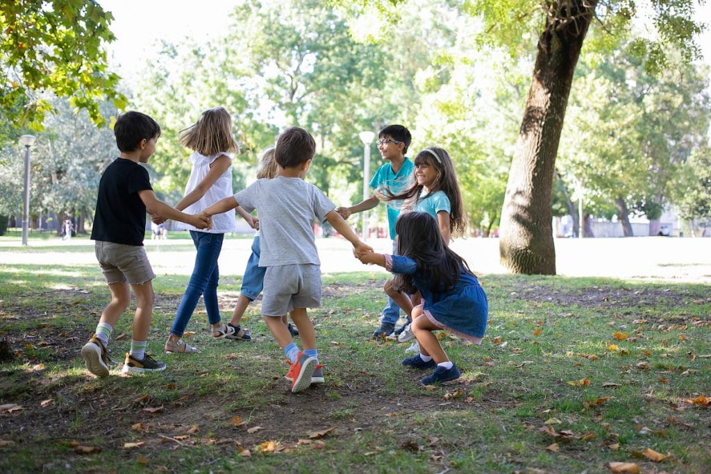 Contato com a natureza beneficia a saúde física e mental das crianças; crianças brincam de mãos dadas em roda em área verde ao ar livre