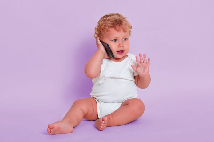 Bebê de fralda sentada no chão fala ao celular