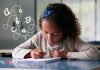 Crianças devem aprender letra cursiva na Era Digital?; crianças sentada em frente a uma mesa escrevendo em um papel com uma caneta