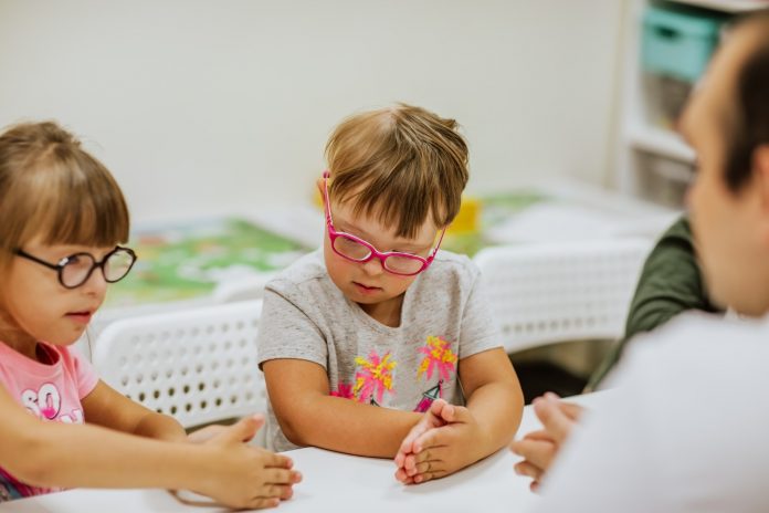Ministro da Educação diz que as crianças com deficiência “atrapalham”; crianças com síndrome de down usando óculos coloridos sentados em frente a uma mesa brincando