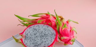Conheça frutas exóticas saborosas para apresentar às crianças; foto de duas pitayas, a da frente está cortada na metade e a de trás está fechada. em cima de uma superfície branco sobre um fundo rosa claro