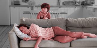 Passar um tempo sem os filhos é necessário, dizem especialistas; mãe cansada deitada no sofá segurando um celular com criança soprando um apito ao fundo
