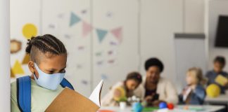 Mãe e especialista em vírus fala sobre volta às aulas com a variante Delta; garoto de máscara lê livro em pé na sala de aula