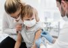 Chile aprova a vacina CoronaVac para crianças com mais de 6 anos; médico com máscara e luvas azuis aplicando vacina em criança pequena no colo da mãe, os dois também usam máscara