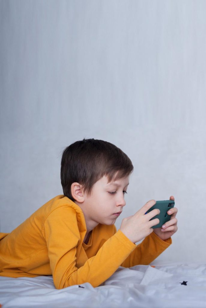 Perigo nas redes: 4 dicas para evitar assédio virtual a crianças; Menino deitado jogando no celular