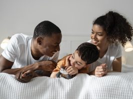 Mãe, pai e filho deitados de bruços na cama; Quando a parentalidade afeta o casal