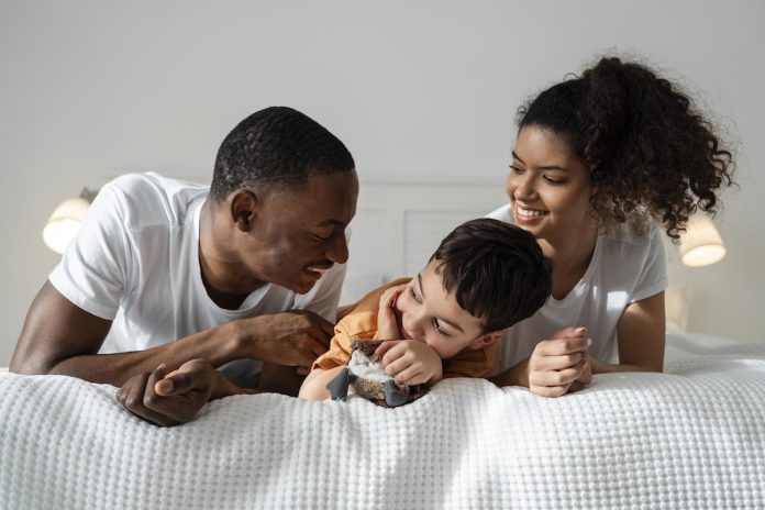 Mãe, pai e filho deitados de bruços na cama; Quando a parentalidade afeta o casal