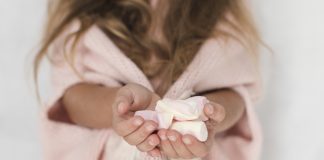 Menina de roupão rosa oferece marshmallow; ingestão de açúcar na infância pode aumentar risco de cáries
