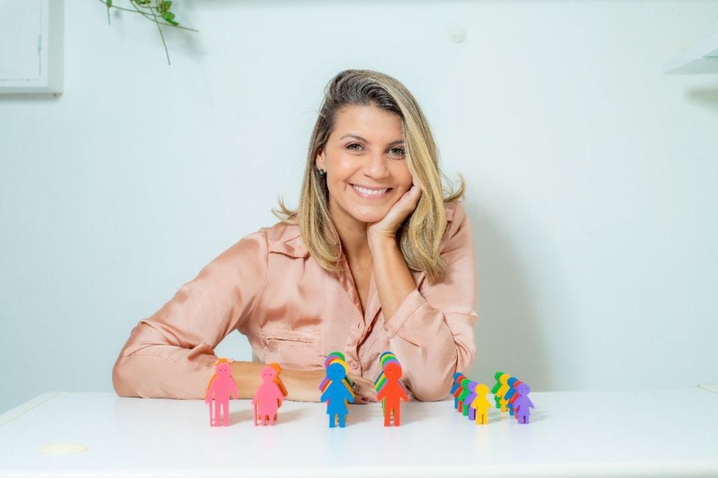 Psicóloga Cristiane Lima apoia braços sobre mesa que tme bonecos coloridos que representam a família