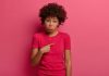 Mulher de blusa vermelha aponta dedo para si mesma; é preciso parar de culpar os pais pelos nossos comportamentos inadequados