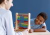A importância de projetos de lei inclusivos para crianças TDAH; criança sorrindo brincando com brinquedo de contagem colorido com uma mulher de costas sorrindo