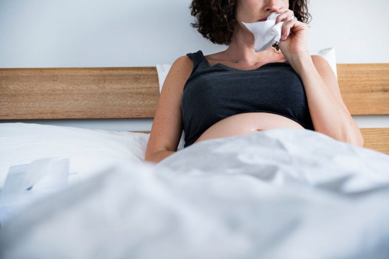 Sobe a letalidade da Covid-19 em gestantes e puérperas; mulher grávida na cama assoando o nariz