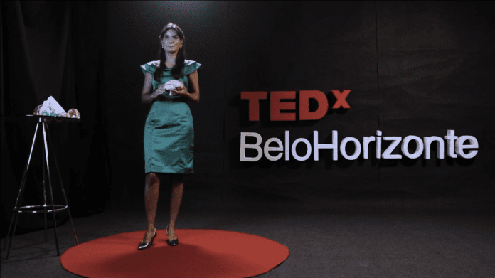 TEDx: como a neurociência pode contribuir para o sucesso das crianças; Liubiana Arantes com vestido verde segurando um cérebro de plástico no TEDx Belo Horizonte