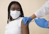 Menina negra de máscara recebe vacina no braço esquerdo