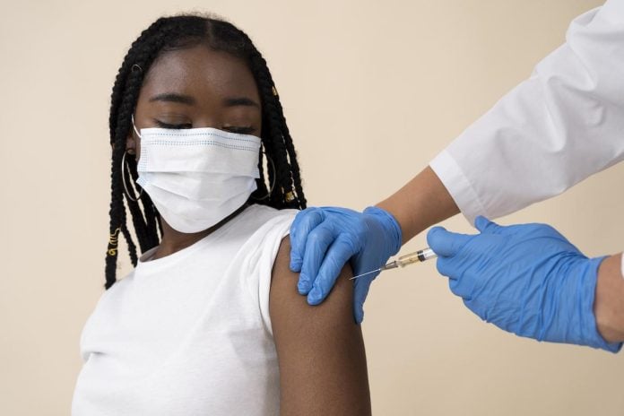 Menina negra de máscara recebe vacina no braço esquerdo