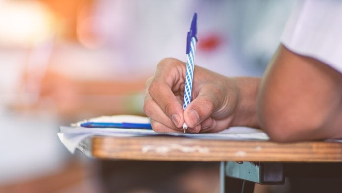 Mão de jovem escreve com caneta sobre papel, uma referência ao vestibular