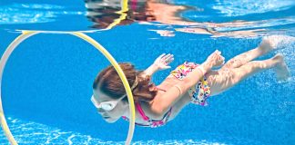 Menina debaixo d'água, dentro de piscina, passa por dentro de bambolê