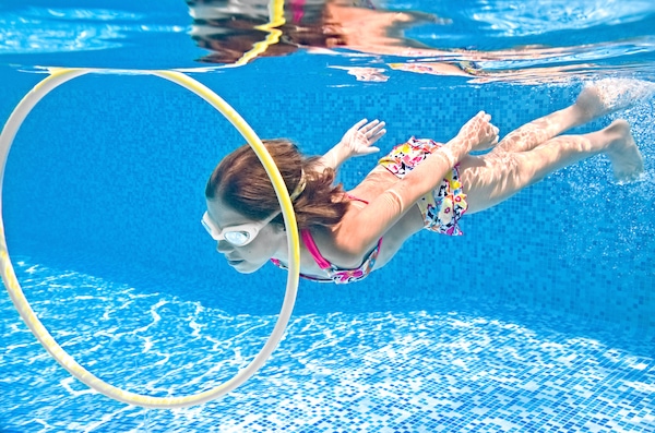 Menina debaixo d'água, dentro de piscina, passa por dentro de bambolê