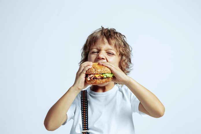 Menino de camiseta branca consumindo alimentos ultraprocessados na infância