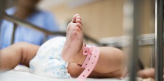 Bebê no berço com pulseira de identificação; Bebês prematuros: quais são as causas para o nascimento antes da hora?