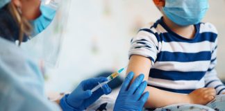 Vacinação contra o coronavírus: e a vez das crianças?; médica de luvas e máscara azuis aplicando vacina em criança de blusa azul listrada usando máscara
