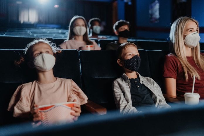 O que assistir com as crianças no cinema em dezembro?; crianças e com a mãe de máscara na sala de cinema