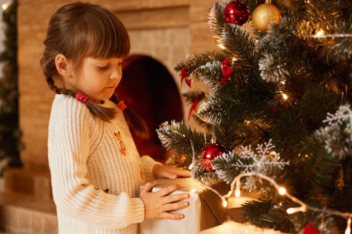 Menina séria mexe em árvore de Natal; Festas de fim de ano podem ser difíceis para as crianças