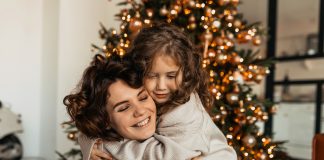 Mãe e filha se abraçam agachadas em frente à árvore de Natal