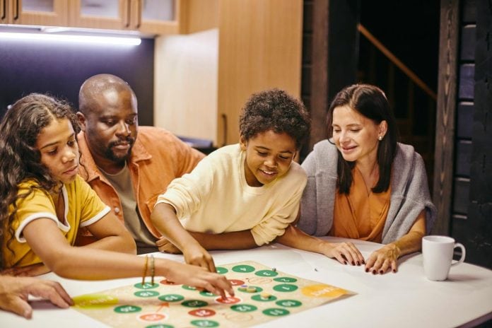 Jogos de tabuleiro para trabalhar o raciocínio e a criatividade das crianças; pai, mãe e filho jogando jogo de tabuleiro em uma mesa