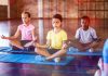 Crianças sentadas, durante prática de mindfulness na escola, com pernas cruzadas e olhos fechados