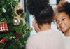 Criança de costas e mãe sorridente olhando apra ele em frente à árvore de Natal