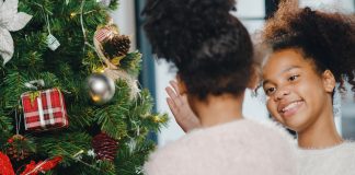 Criança de costas e mãe sorridente olhando apra ele em frente à árvore de Natal
