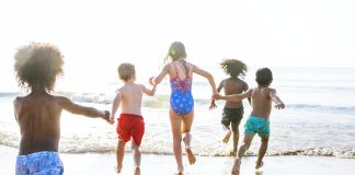 Na praia, cinco crianças correm para entrar no mar