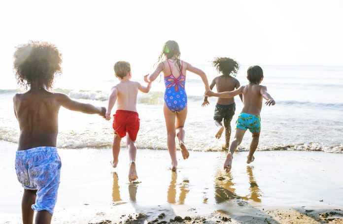 Na praia, cinco crianças correm para entrar no mar