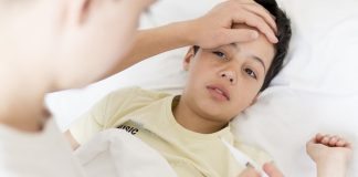Adulto apoia mão na testa de menino e olha para termômetro na outra mão; Surto de gripe em SP: crescem casos em crianças