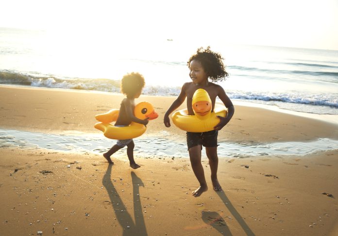 Irmãos com boia amarela de patinho na cintura brincam na areia