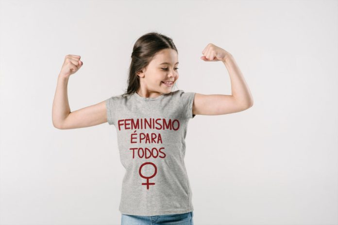 Criança feminista com os braços dobrados, mostrando força, usando camiseta com a frase 