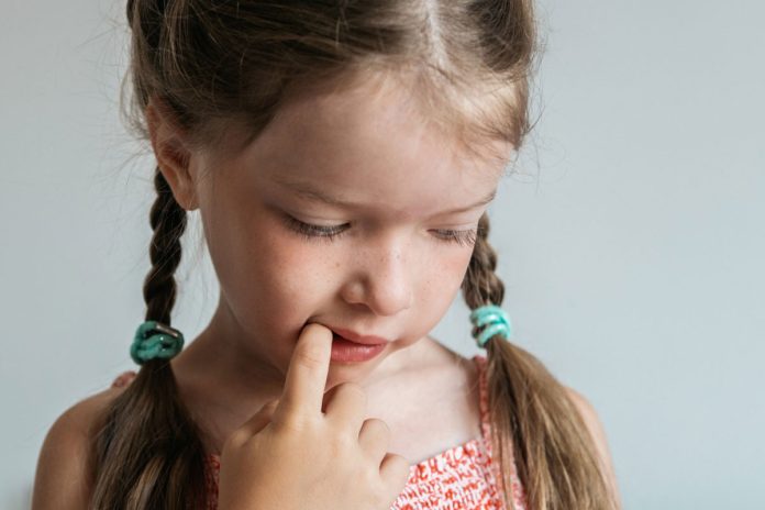 Menina com o hábito de roer as unhas na infância com o dedo na boca