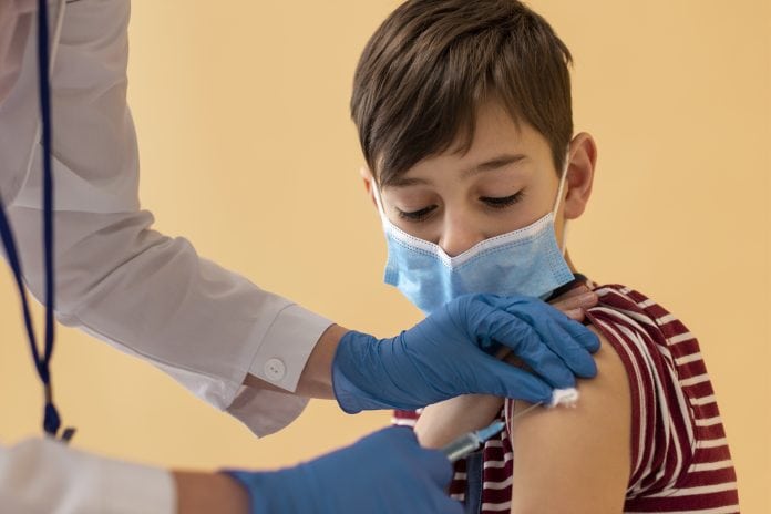 Especialistas esclarecem dúvidas sobre vacinação de crianças; criança de máscara tomando vacina