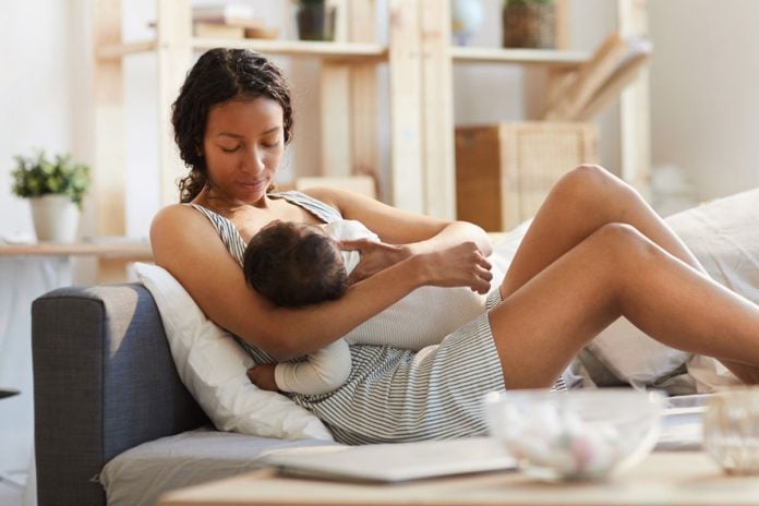 Mãe amamentando bebê sentada no sofá