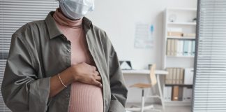 Mulher grávida de máscara segurando a barriga, protegida contra a covid em grávidas