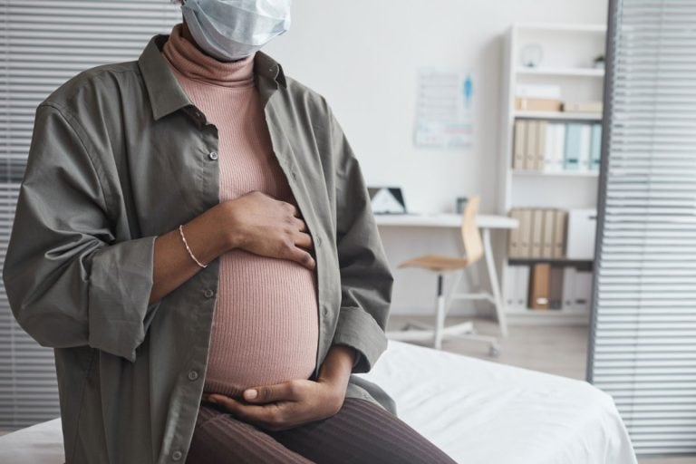 Mulher grávida de máscara segurando a barriga, protegida contra a covid em grávidas