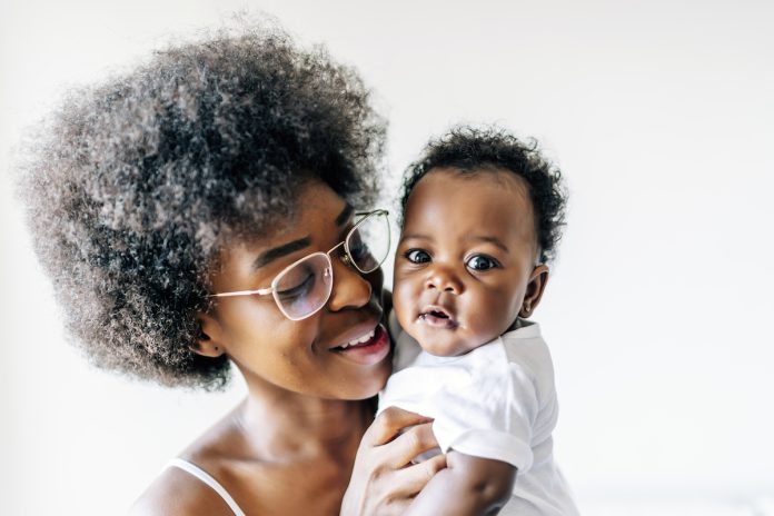 Mãe negra de óculos segura bebê no braço