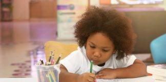 Menina de cabelo crespo pinta desenho em papel
