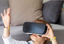 Menina com óculos de realidade virtual (VR) sentada no chão da sala com mão estendida