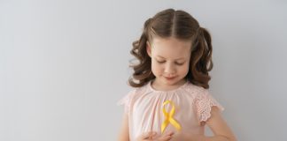 Menina segura fita de cetim amarela em referência ao Dia Internacional de Câncer Infantil