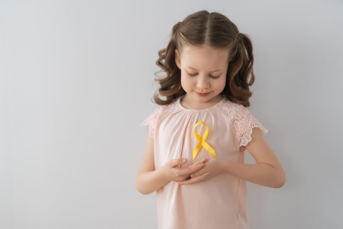 Menina segura fita de cetim amarela em referência ao Dia Internacional de Câncer Infantil