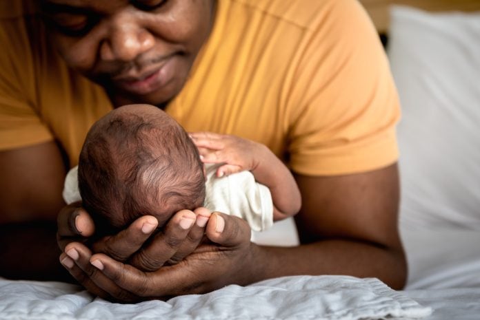 Pai negro está deitado e segura recém-nascido nos braços